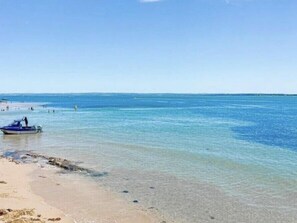 Une plage avec une eau claire et peu profonde, un bateau sur le rivage et des gens dans l’eau.