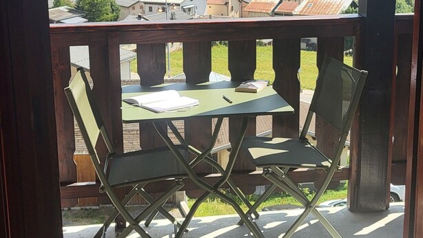 A balcony with two green folding chairs and a table, overlooking a town and mountains. - Aussois le bon choix - Apartment at the foot of the pistes, south facing, sleeps 5 (Aussois)