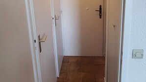 A narrow hallway with white walls and brown tiled flooring, leading to a closed door. - Aussois le bon choix - Apartment at the foot of the pistes, south facing, sleeps 5 (Aussois)