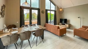 Ein modernes Wohnzimmer mit Essbereich, großen Fenstern und einem Flachbildfernseher.