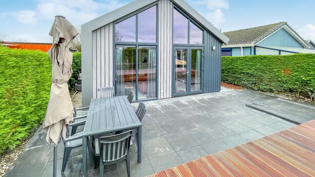 Ein modernes Haus mit einer großen Glasdoor und einer Terrasse, komplett mit Tisch und Stühlen.