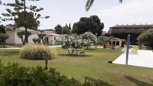 A courtyard with a variety of trees and shrubs, a paved walkway, and a building with a tiled roof in the background. - Chalet located on a wooded park of 8000m ² with large community pool, . (Vilafortuny)