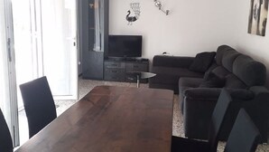 A living room with a dark brown wooden dining table, a dark grey sofa, and a flat-screen TV on a stand. - Chalet located on a wooded park of 8000m ² with large community pool, . (Vilafortuny)