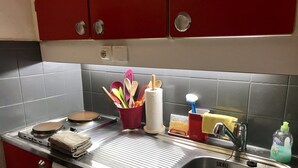 Keittiössä on ruostumattomasta teräksestä valmistettu pesuallas, punaiset kaapit ja erilaisia keittiövälineitä punaisessa kupissa.