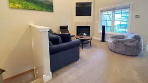 Ein Wohnzimmer mit Sofa, Sessel, Couchtisch, Kamin und einem großen Fenster.
