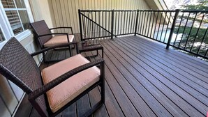 Eine überdachte Terrasse mit dunklem Holzboden, Metallgeländer und Korbmöbeln mit Kissen.