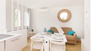 A modern, well-lit room with a dining table set for four, a sofa with cushions, and a round mirror on the wall.