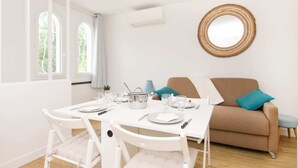 A dining area with a table set for two, a sofa, and a wall-mounted mirror.