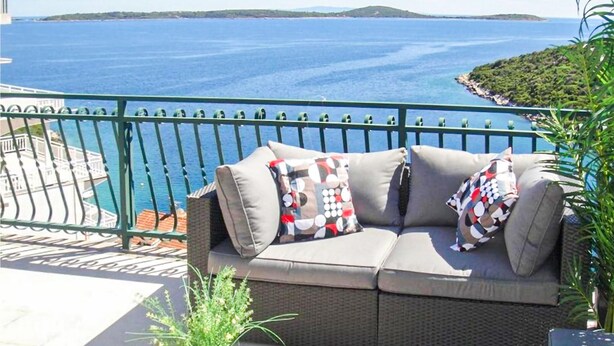 A balcony with a wicker sofa and cushions, overlooking a body of water and a distant landmass. - 2 bedroom amazing apartment in Vinisce (Vinisce)