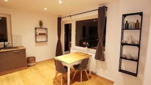 A compact kitchen with a dining area, wooden flooring, a window with curtains, and a shelf with kitchenware. - House on the terp, vacation apartment#1 ground floor (Pogum)