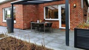 A patio with a table and chairs, a brick house, and a glass enclosure. - House on the terp, vacation apartment#1 ground floor (Pogum)