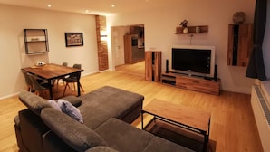 A modern living room with a large flat-screen TV, a wooden dining table, and a grey sofa. - House on the terp, vacation apartment#1 ground floor (Pogum)
