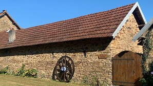 A stone building with a red-tiled roof, a large wooden wheel, and a wooden gate. - French Gite on Dordogne border with private pool (Saint-Yrieix-la-Perche)