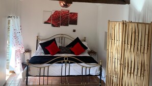 Una habitación con cama, techo de madera, separador de bambú y una pared con obras de arte.