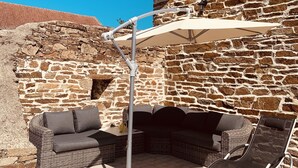 Edificio de piedra con patio empedrado, mobiliario exterior y una pérgola que ofrece sombra.