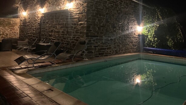 Un edificio de piedra con piscina, sillas de descanso y un muro de piedra.