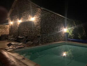 Un bâtiment en pierre doté d’une piscine, de chaises longues et d’un mur en pierre.
