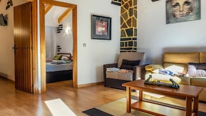 Una sala de estar acogedora con piso de madera, un sofá, una mesita de centro y una cama con vistas a través de un ventanal abierto.