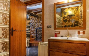 Enter a bathroom with rustic charm, featuring a stone wall, a large mirror, and a white sink with a gold faucet.