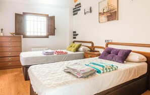 Two beds and a dresser in a cozy room with a window offering a view of the outside.