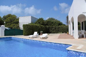 A swimming pool with lounge chairs, a green gate, and a white building with arches.