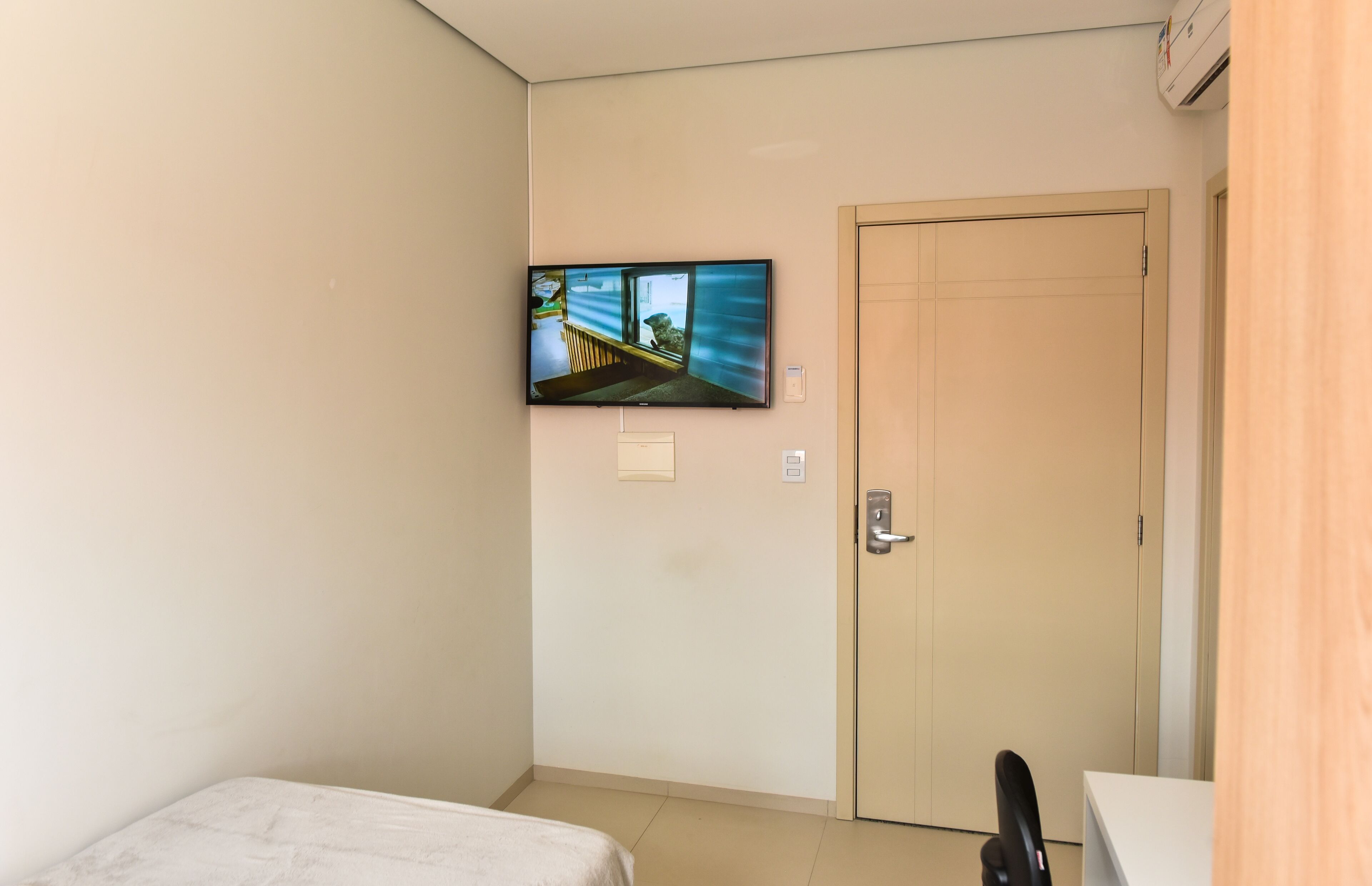 Una habitación de hotel con una cama, un televisor montado en la pared, una puerta y un escritorio.