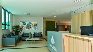 Un área de recepción moderna con un mostrador de madera, dos sofás grises, una pequeña mesa redonda y una pared verde.