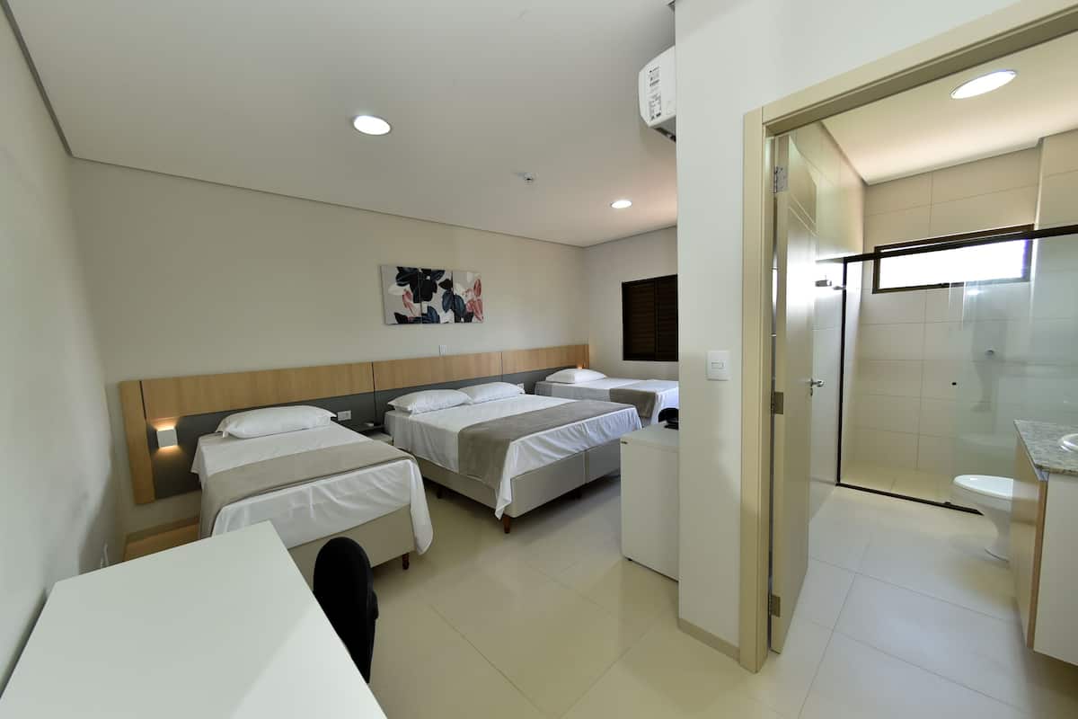A hotel room with two beds, a desk, a small table, a shower area, and a bathroom.