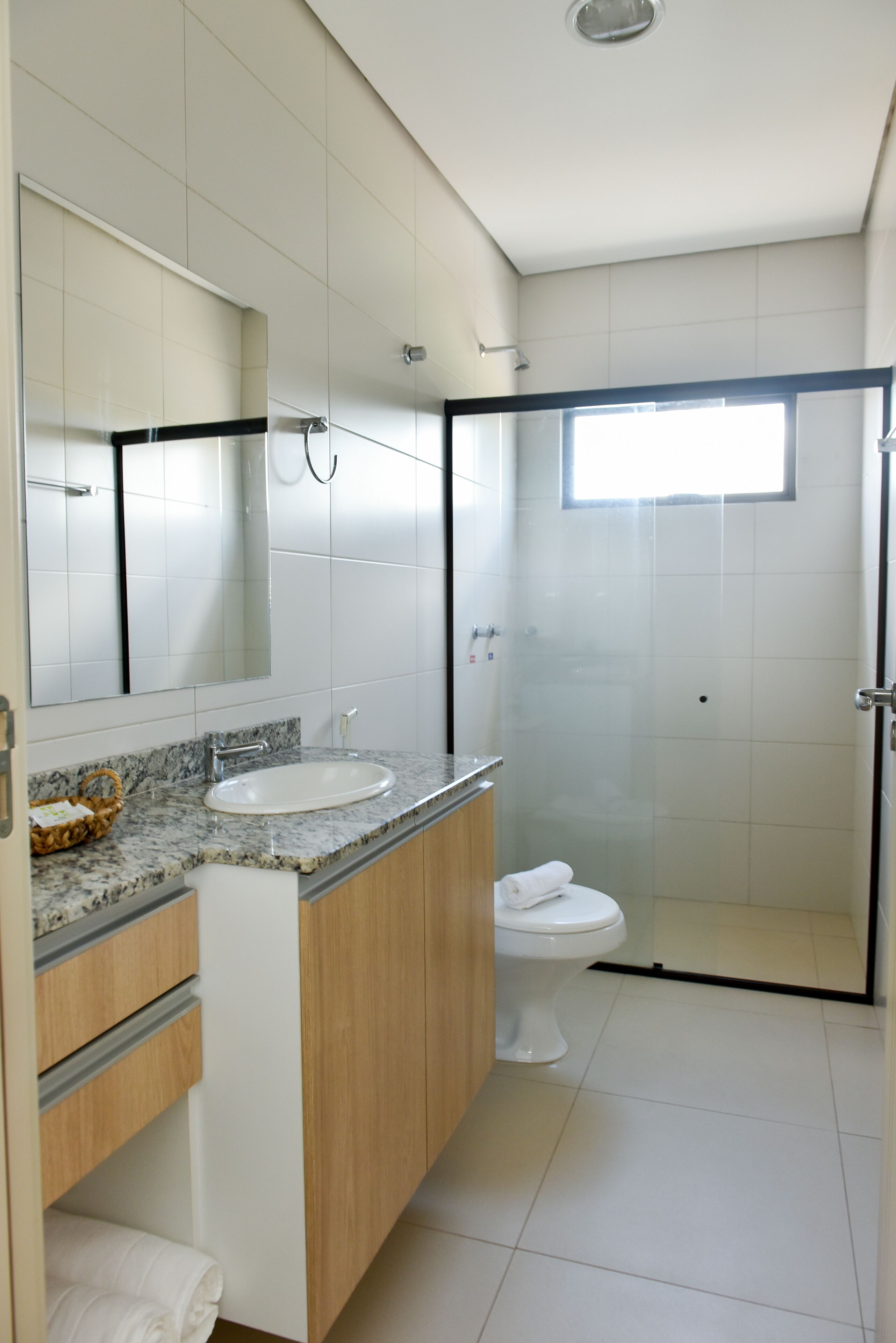 A modern bathroom with a marble sink, wooden cabinets, a glass shower enclosure, and a large mirror.