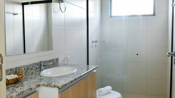 A modern bathroom with a marble sink, wooden cabinets, a glass shower enclosure, and a large mirror.