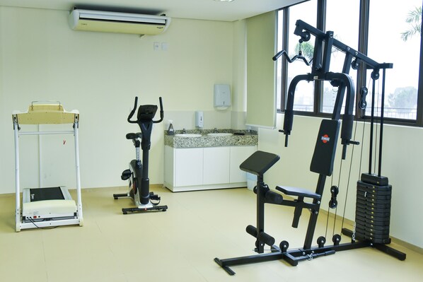 Un gimnasio con equipo de cardio, una banca de pesas y un ventanal.