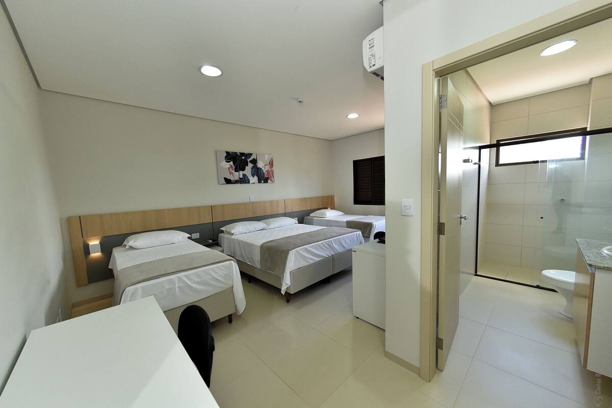 A hotel room with three single beds, a desk, a mirror, and a small kitchenette.