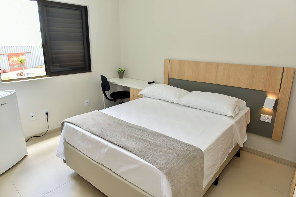 A bedroom with a bed, a desk, a chair, and a window.