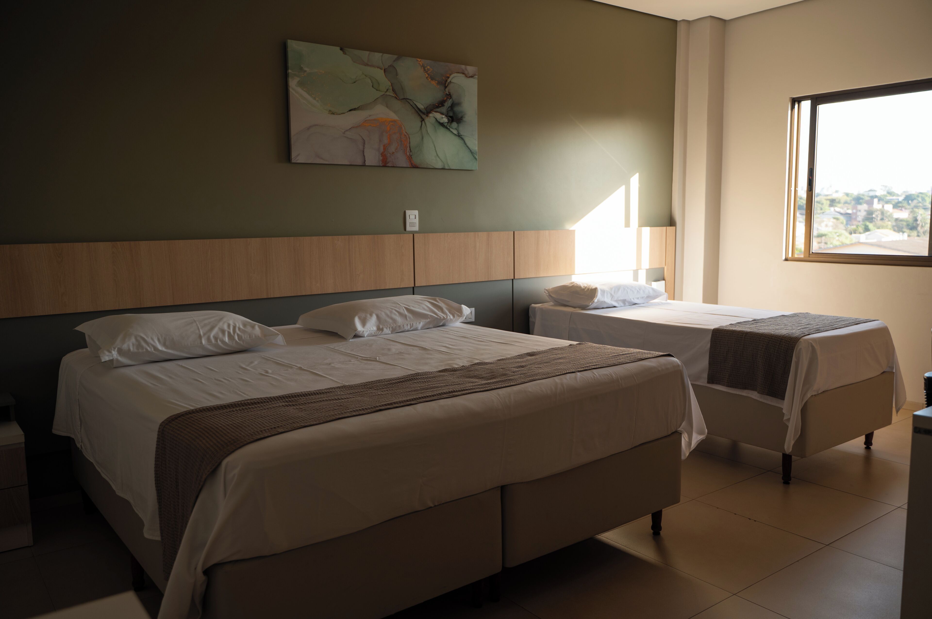 Ein Hotelzimmer mit zwei Betten, einem großen Fenster und einem an der Wand hängenden abstrakten Gemälde.