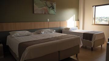 Ein Hotelzimmer mit zwei Betten, einem großen Fenster und einem an der Wand hängenden abstrakten Gemälde.