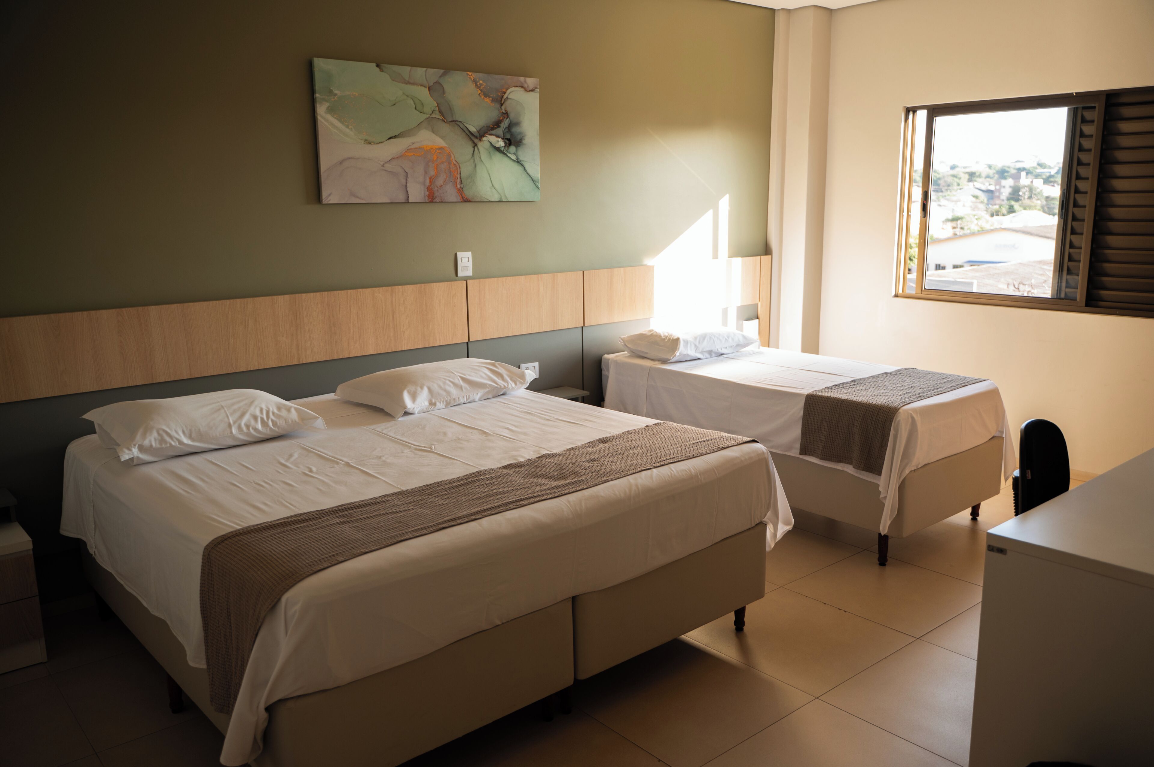 Habitación de hotel con dos camas, un escritorio, una ventana y un cuadro en la pared.