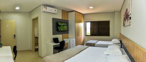 A hotel room with two beds, a desk with a laptop, a television, and a window with blinds.
