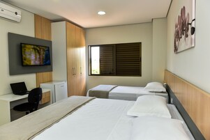 Habitación de hotel con dos camas, un escritorio con una computadora portátil, un televisor y una ventana con persianas.