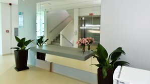 Una recepción con un separador de vidrio, plantas en macetas y una escalera al fondo.