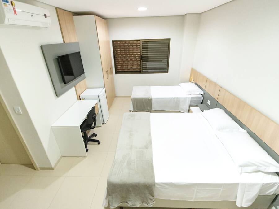 Habitación de hotel con dos camas, un escritorio, un televisor y una ventana con persianas.