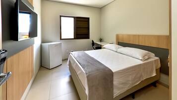 A bedroom with a bed, a desk, a chair, a TV, and a window.
