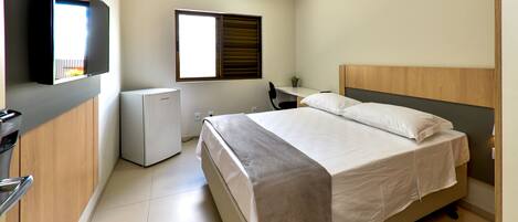 Un dormitorio con cama, escritorio, silla, televisor y ventana.