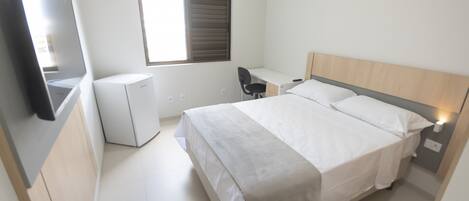 Un dormitorio con cama, escritorio, silla, televisor y ventana.