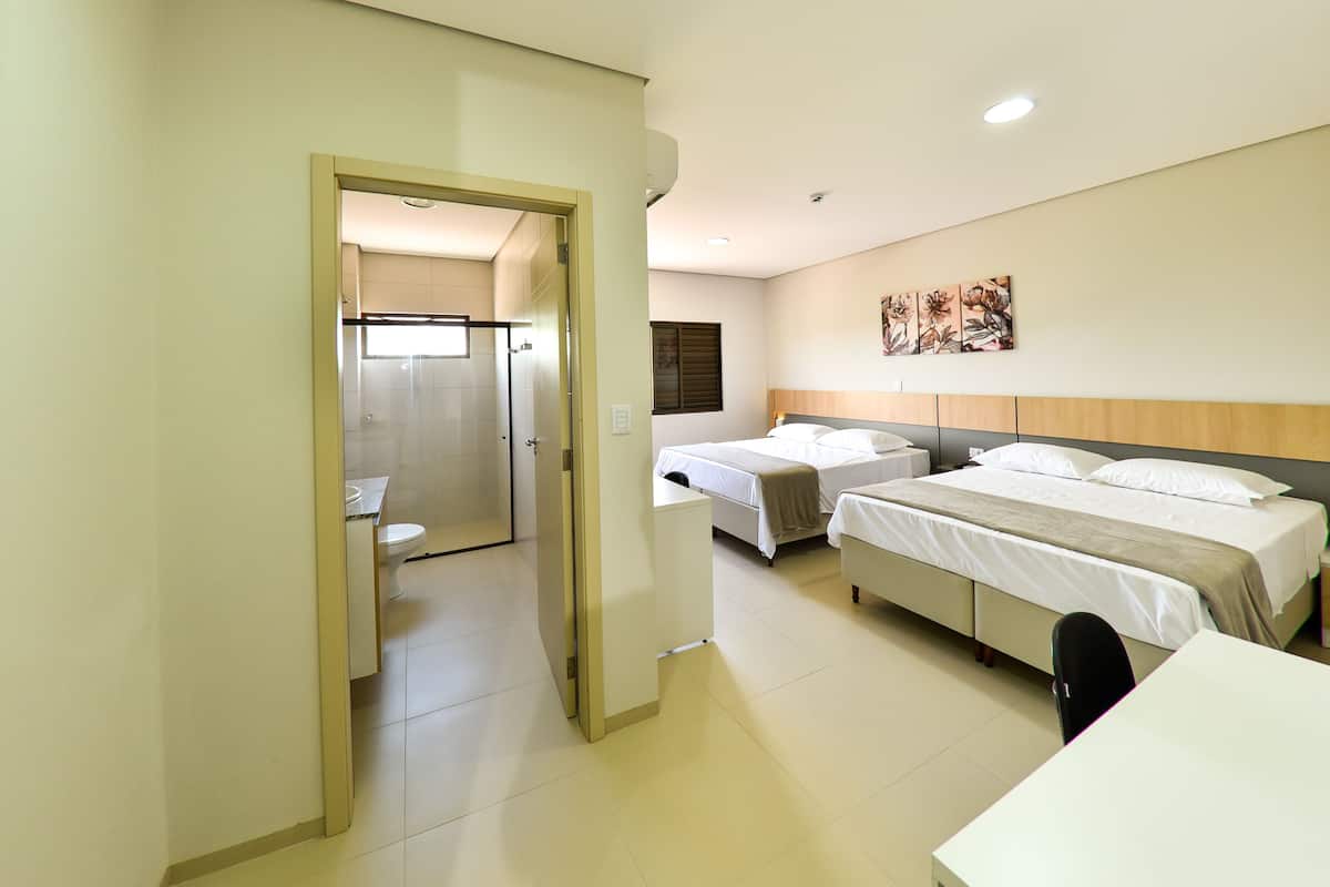 A hotel room with two beds, a desk, and a bathroom visible through an open door.