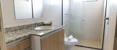 A modern bathroom with a marble countertop, a large mirror, a toilet, and a glass-enclosed shower.
