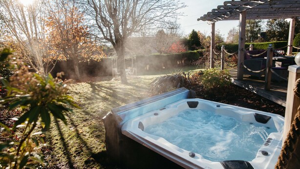 Een hottub in een tuin met een pergola en een zitgedeelte.