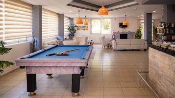 A pool table in a well-lit room with a sofa, chairs, and a bookshelf.