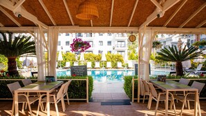 An outdoor patio with tables and chairs, a pool in the background, and a sign indicating food and beverages are allowed. - Nora Suit Hotel (Manavgat)