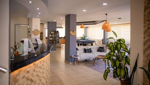 A modern hotel lobby with a reception desk, seating area, and a bookshelf. - Nora Suit Hotel (Manavgat)