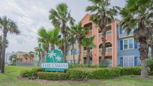 A sign for The Dawn Condominiums with a tropical theme, surrounded by palm trees and a well-maintained lawn. - <br>The Dolphin Poolside at The Dawn. (Galveston)